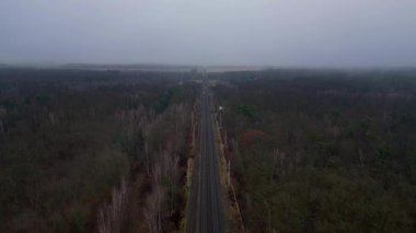 Demiryolu manzarası bulutlu gökyüzü altındaki büyük ormanı geçerek karamsar ve atmosferik manzaralar yaratıyor. Ters İHA uçuşu 