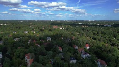 Hayır, Berlin 'de bir yerleşim bölgesi. Yoğun bir ormanın içine yerleştirilmiş evler var. Ufukta şehrin ufku görünüyor. Ters İHA uçuşu 