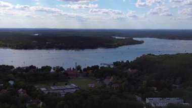 Wannsee göllerinde gezinen yelkenliler, güneşli bir günde, mavi gökyüzü ve bulutlarla çevrili yemyeşil ormanlarla çevrilidir. Sağ drona döndür 