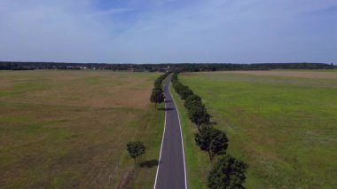 Ağaçlar ve tarlalarla dolu kırsal bir araziden geçen boş bir asfalt yolun havadan görünüşü. İHA 'yı çek 