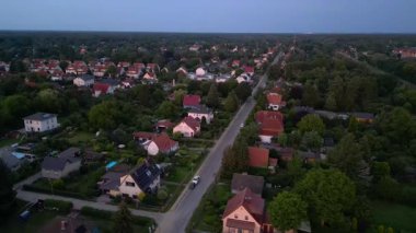 Brandenburg, Almanya 'da sakin bir akşam, çatıların, yemyeşil otlakların ve bir yol ağının sergilendiği bir yerleşim alanına iniyor. geniş yörünge görünümü dronu 