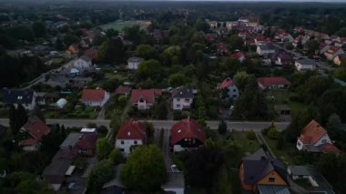Brandenburg, Almanya 'da sakin bir akşam, çatıların, yemyeşil otlakların ve bir yol ağının sergilendiği bir yerleşim alanına iniyor. panorama yörünge dronu 