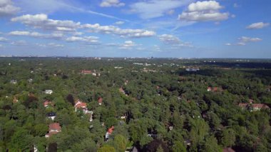 Hayır, Berlin 'de bir yerleşim bölgesi. Yoğun bir ormanın içine yerleştirilmiş evler var. Ufukta şehrin ufku görünüyor. panorama genel görünüm dronu 