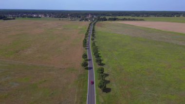Asfalt bir yolda, ağaçlar ve tarlalarla dolu kırsal bir araziden geçen bir arabanın hava görüntüsü. panorama genel görünüm dronu 