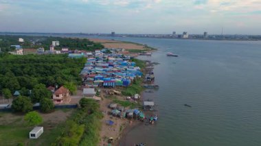 Güneydoğu Asya 'da gelişmekte olan bir ülke olan Kamboçya' daki Mekong nehri boyunca renkli kulübeleri olan bir balıkçı köyünün hava manzarası. Yukarıdan aşağıya uçan vinç drone 'u 