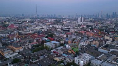 Bangkok üzerinde turuncu gün batımı çatıları ve binaları aydınlatıyor. Yukarıdan aşağıya doğru uçur 