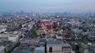 Geleneksel ve modern binaların arasında öne çıkan altın bir Chedi 'nin yer aldığı gün batımında Bangkok şehir manzarası. Ters İHA uçuşu 