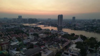 Bangkok üzerinde turuncu gün batımı çatıları ve binaları aydınlatıyor. İHA yükseliyor 