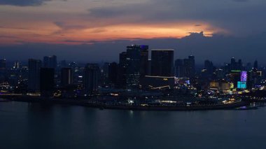 Phnom Penh 'in modern binaları, turuncu bulutlarla Mekong Nehri' nde günbatımını yansıtıyor. Yukarıdan insansız hava aracı görüntüleri 