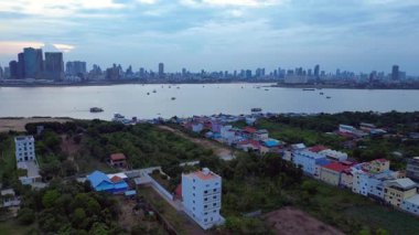 Mekong Nehri 'nin karşısındaki Phnom Penh' in modern şehir manzarasıyla çelişen kırsal bir köydeki hareketli bir sokak pazarının havadan görünüşü. hız rampası hiper hareket zaman aşımı 