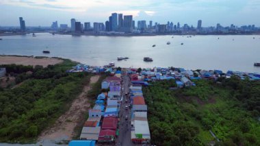 Mekong Nehri 'nin karşısındaki Phnom Penh' in modern şehir manzarasıyla çelişen kırsal bir köydeki hareketli bir sokak pazarının havadan görünüşü. panorama genel görünüm dronu 