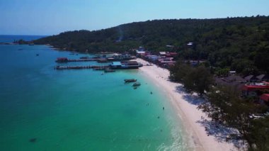 Kristal berrak turkuaz suları, beyaz kumlu plajı ve kıyı şeridi boyunca uzanan canlı bir balıkçı köyü olan Koh Rong adası. İHA alçalıyor 