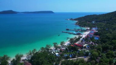 Kristal berrak turkuaz suları, beyaz kumlu plajı ve kıyı şeridi boyunca uzanan canlı bir balıkçı köyü olan Koh Rong adası. panorama genel görünüm dronu 