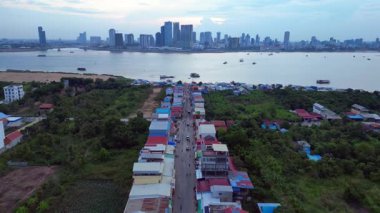 Mekong Nehri 'nin karşısındaki Phnom Penh' in modern şehir manzarasıyla çelişen kırsal bir köydeki hareketli bir sokak pazarının havadan görünüşü. İticileri ileri çalıştır 