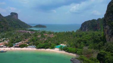 Railay Sahili 'nde ünlü kireçtaşı kayalıkları, yemyeşil alanları ve Andaman Denizi' nin canlı turkuaz suları sergileniyor. Sağ drona döndür 