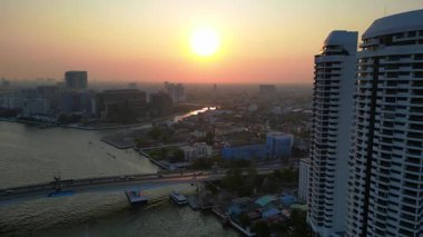 Chao Phraya Nehri, günbatımında, modern binalar ve Tayland 'da köprü ile denize açılan teknelerle. Ters İHA uçuşu 