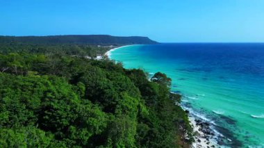 Turkuaz sudaki siyah taşlar açık mavi gökyüzüyle güneşli bir günde Kamboçya 'nın Koh Rong adasının beyaz kumsalını nazikçe yıkıyor. panorama genel görünüm dronu 