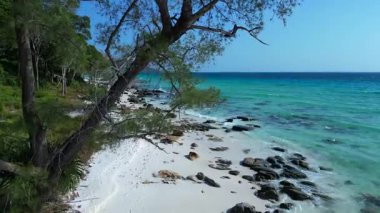 Turkuaz sudaki siyah taşlar açık mavi gökyüzüyle güneşli bir günde Kamboçya 'nın Koh Rong adasının beyaz kumsalını nazikçe yıkıyor. İHA alçalıyor 