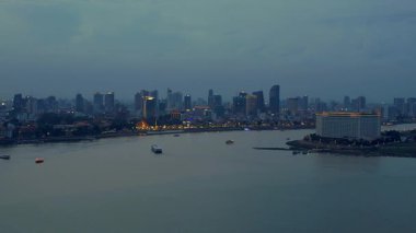 Phnom Penh ufuk çizgisi üzerinde gün batımı aydınlatılmış köprüyle birlikte tur botlarıyla Mekong Nehri 'ni geçiyor. panorama genel görünüm dronu 