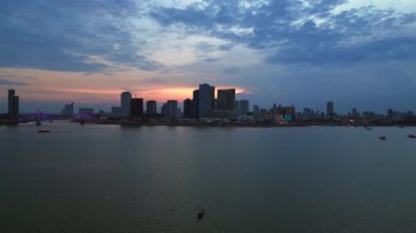 Phnom Penh ufuk çizgisi üzerinde gün batımı aydınlatılmış köprüyle birlikte tur botlarıyla Mekong Nehri 'ni geçiyor. İHA alçalıyor 