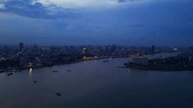 Phnom Penh ufuk çizgisi üzerinde gün batımı aydınlatılmış köprüyle birlikte tur botlarıyla Mekong Nehri 'ni geçiyor. Yukarıdan insansız hava aracı görüntüleri 