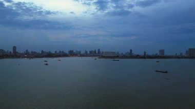 Phnom Penh ufuk çizgisi üzerinde gün batımı aydınlatılmış köprüyle birlikte tur botlarıyla Mekong Nehri 'ni geçiyor. Sağ drona döndür 