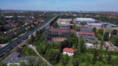 Berlin, Almanya 'da mavi bir gökyüzünün altında ağaçlar ve binalarla çevrili bir gaz sayacının hava görüntüsü. Yukarıdan insansız hava aracı görüntüleri 