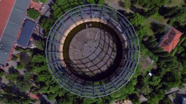 Berlin, Almanya 'da mavi bir gökyüzünün altında ağaçlar ve binalarla çevrili bir gaz sayacının hava görüntüsü. dikey kuş bakışı dron 