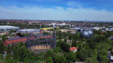 Berlin, Almanya 'da mavi bir gökyüzünün altında ağaçlar ve binalarla çevrili bir gaz sayacının hava görüntüsü. panorama genel görünüm dronu 