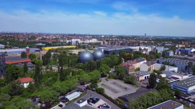 İki küresel gaz ölçer, Berlin şehir manzarasının ortasında, parlak bir yaz gününde kentsel enerji ve sanayi mirasını yakalıyor. panorama genel görünüm dronu 
