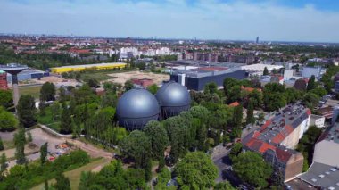 İki küresel gaz ölçer, Berlin şehir manzarasının ortasında, parlak bir yaz gününde kentsel enerji ve sanayi mirasını yakalıyor. Yukarıdan insansız hava aracı görüntüleri 