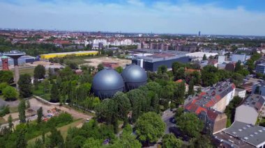 İki küresel gaz ölçer, Berlin şehir manzarasının ortasında, parlak bir yaz gününde kentsel enerji ve sanayi mirasını yakalıyor. Ters İHA uçuşu 