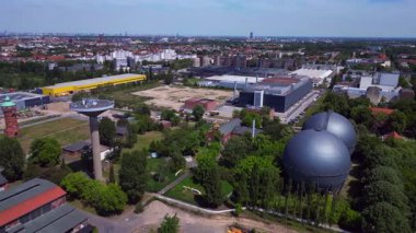İki küresel gaz ölçer, Berlin şehir manzarasının ortasında, parlak bir yaz gününde kentsel enerji ve sanayi mirasını yakalıyor. panorama genel görünüm dronu 