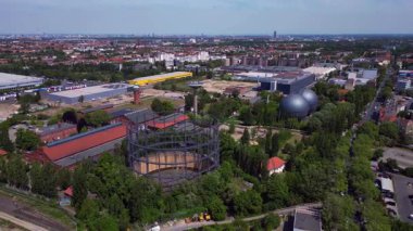 Berlin, Almanya 'da mavi bir gökyüzünün altında ağaçlar ve binalarla çevrili bir gaz sayacının hava görüntüsü. panorama yörünge dronu 