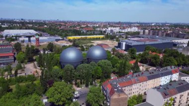 İki küresel gaz ölçer, Berlin şehir manzarasının ortasında, parlak bir yaz gününde kentsel enerji ve sanayi mirasını yakalıyor. panorama yörünge dronu 