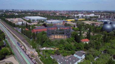Berlin, Almanya 'da mavi bir gökyüzünün altında ağaçlar ve binalarla çevrili bir gaz sayacının hava görüntüsü. panorama genel görünüm dronu 