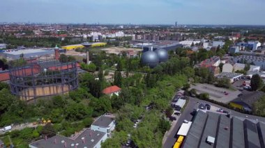 Berlin, Almanya 'da mavi bir gökyüzünün altında ağaçlar ve binalarla çevrili bir gaz sayacının hava görüntüsü. panorama genel görünüm dronu 