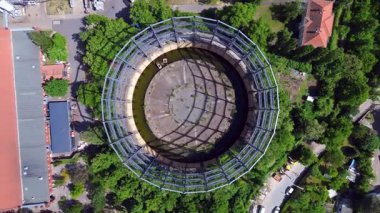 Berlin, Almanya 'da mavi bir gökyüzünün altında ağaçlar ve binalarla çevrili bir gaz sayacının hava görüntüsü. Sol İHA 'ya dön 