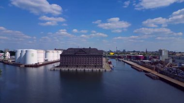 Berlin Westhafen endüstriyel limanının arka planında yakıt depolama tankları, kargo konteynerleri ve Berlin şehir manzarası var. İHA alçalıyor 