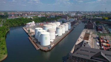 Berlin Westhafen endüstriyel limanının arka planında yakıt depolama tankları, kargo konteynerleri ve Berlin şehir manzarası var. statik üç ayaklı insansız hava aracı 