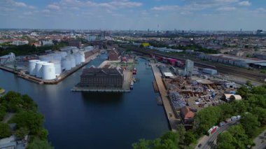 Berlin Westhafen endüstriyel limanının arka planında yakıt depolama tankları, kargo konteynerleri ve Berlin şehir manzarası var. panorama genel görünüm dronu 