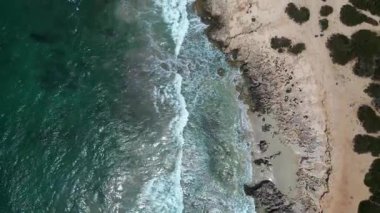 Turkuaz dalgalar ses Salines sahilinin kayalık sahillerine antik gözetleme kulesiyle çarpıyor. dikey kuş bakışı dron 