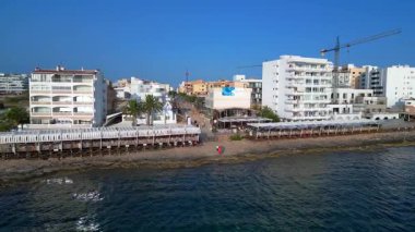 Turistler yaz tatillerini San Antonio Körfezi, İbiza 'da ünlü bir bar olan Cafe del Mar' da geçiriyorlar. panorama yörünge dronu 