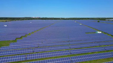 Sıralar halinde fotovoltaik güneş panelleri açık mavi gökyüzünün altındaki büyük bir enerji istasyonunda güneşi emiyor. Yukarıdan insansız hava aracı görüntüleri 