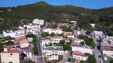 İspanya 'nın İbiza kentindeki Sant Joan de Labritja' da, güneşli bir yaz gününde geleneksel beyaz kilise, evler, yollar, dağlar ve yemyeşil alanlar yer alıyor. İHA yükseliyor 