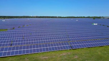Sıralar halinde fotovoltaik güneş panelleri açık mavi gökyüzünün altındaki büyük bir enerji istasyonunda güneşi emiyor. panorama genel görünüm dronu 