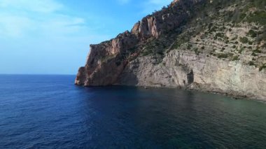 İspanya 'nın İbiza kentindeki bir körfezdeki kayaların arasından şeffaf turkuaz su akar. Yukarıdan insansız hava aracı görüntüleri 