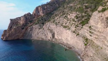 İspanya 'nın İbiza kentindeki bir körfezdeki kayaların arasından şeffaf turkuaz su akar. İHA alçalıyor 