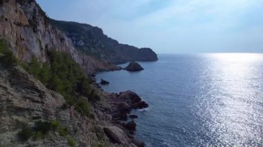 İspanya 'nın İbiza kentindeki bir körfezdeki kayaların arasından şeffaf turkuaz su akar. Ters İHA uçuşu 