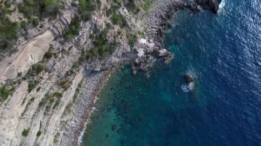 İspanya 'nın İbiza kentindeki bir körfezdeki kayaların arasından şeffaf turkuaz su akar. Drone 'u yukarı eğ 
